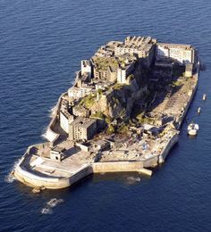 an island in the middle of the ocean with buildings on it and boats floating around