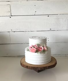 a three tiered white cake with pink flowers on top sitting on a wooden stand