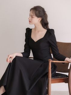 a woman sitting in a chair wearing a black dress