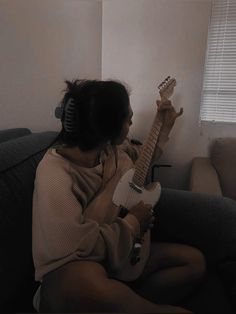 a person sitting on a couch with a guitar in their hand and headphones to their ears