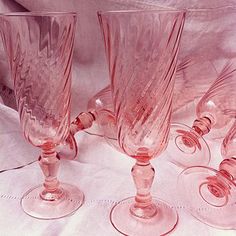 four pink wine glasses sitting on top of a white cloth