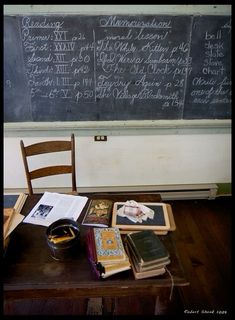 an old desk with books on it in front of a chalkboard that has writing on it