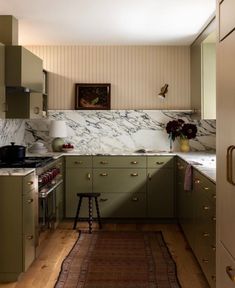 a kitchen with green cabinets and marble counter tops, along with a rug on the floor