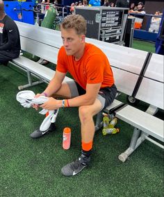 a man in an orange shirt sitting on a bench with his feet up and holding a white frisbee