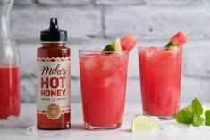 two glasses filled with watermelon and limeade next to a bottle of make's hot honey