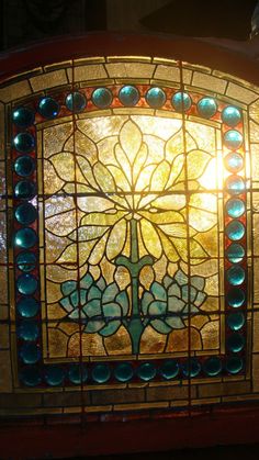 a stained glass window with blue and green beads on it's sides, in front of a light fixture