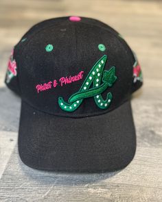 a black hat with green and pink flowers on it, sitting on a wooden surface