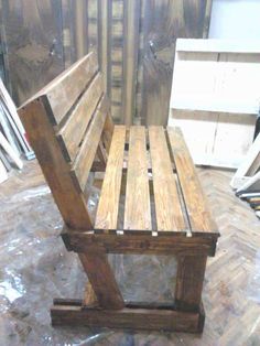 a wooden bench sitting on top of a hard wood floor next to a pile of pallets