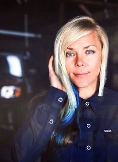 a woman with blonde hair and blue eyes is posing for a photo in front of a car