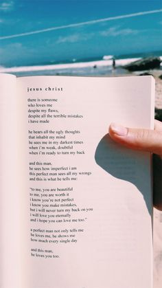 a person holding an open book in their hand on the beach with blue sky and water behind them