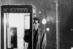 a man standing next to a phone booth in the rain