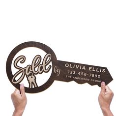 two hands holding up a wooden sign that says sold and the word, olvia ellis