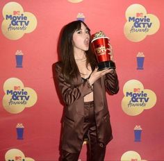 a woman holding up a popcorn bucket in front of a red wall with the words movie and tv awards written on it