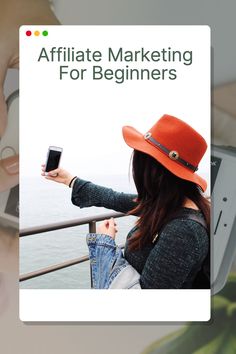 a woman holding a cell phone in her right hand and looking at the screen while wearing a bright orange hat