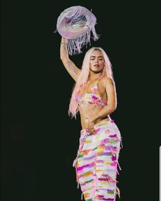 a woman in a colorful skirt holding a hat on top of her head while standing next to a black background