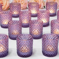 many purple glass cups are lined up next to each other on a table with roses in the background