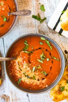 two bowls of tomato soup with bread and parsley on the side for garnish