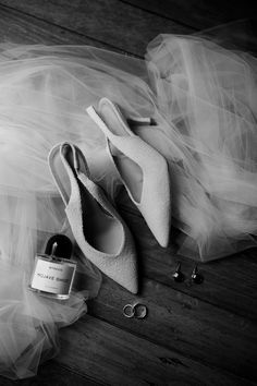 a pair of white shoes sitting on top of a wooden floor next to a bottle of wine