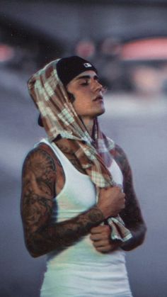 a woman with tattoos wearing a white tank top and a plaid scarf over her head