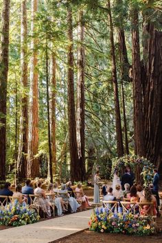 an outdoor ceremony in the woods with people sitting on benches and flowers around them, surrounded by tall trees