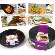 two black pans with food in them on top of a white table and pictures behind them