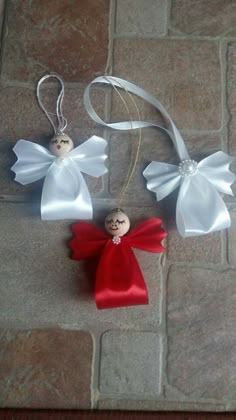 two christmas ornaments on a stone floor with ribbon hanging from the top and an ornament in the middle