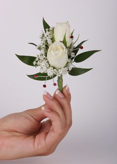 a woman's hand holding a white rose and baby's breath boutonniere