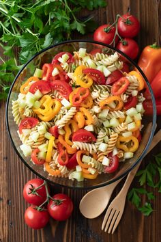 a glass bowl filled with pasta salad next to tomatoes, parsley and other vegetables