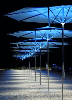 rows of umbrellas lit up at night in an empty parking lot with no people