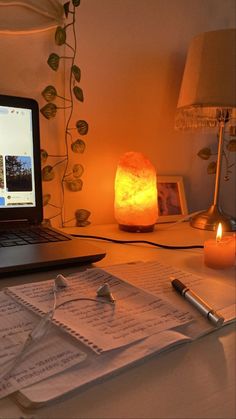 an open laptop computer sitting on top of a desk next to a lamp and papers