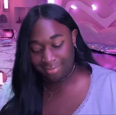 a woman with long black hair looking down at her cell phone while sitting on a bed