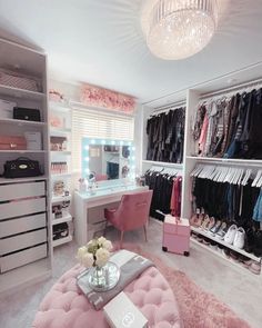 a pink ottoman in front of a dressing room with clothes on shelves and a chandelier hanging from the ceiling