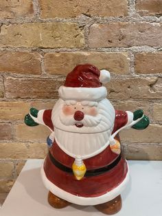 a ceramic santa clause figurine sitting on top of a white table next to a brick wall