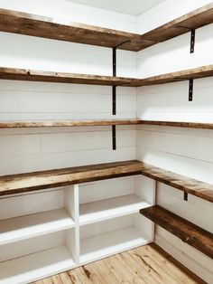 empty shelves in the corner of a white room with wood flooring and shelving