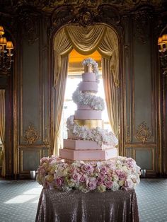 a large pink and gold wedding cake on top of a table in front of a window