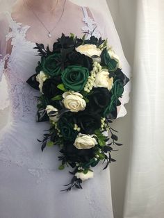 the bride's bouquet is made up of white and green flowers, greenery, and black leaves