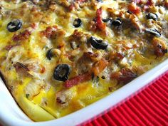 a casserole dish with black olives and meat in it on a red cloth