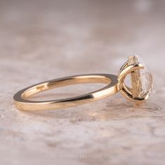 a yellow gold engagement ring with an oval cut diamond in the center, sitting on a marble surface