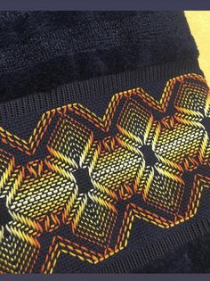 a close up of a knitted object on a yellow table cloth with an orange and black design