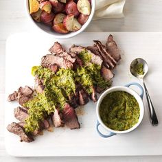 a white cutting board topped with meat and veggies next to a bowl of pesto