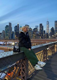 a woman sitting on the edge of a bridge in front of a cityscape