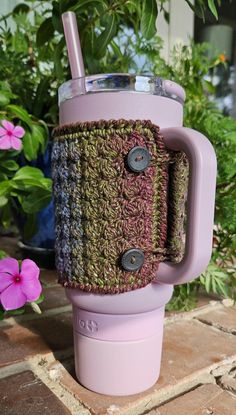 a cup holder with a straw in it on a table next to flowers and potted plants