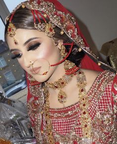 a woman in a red and gold bridal outfit with jewelry on her head, looking at the camera