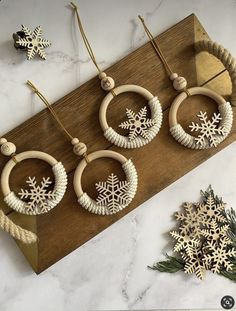 three snowflake wood hoop earrings on a wooden board next to christmas decorations and pine cones