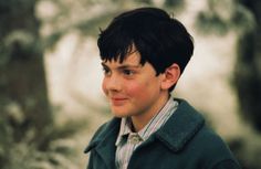 a young boy is standing in front of a tree and looking off into the distance