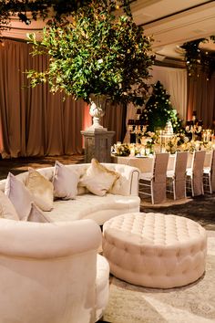 a room filled with white couches and tables covered in greenery next to a tall tree