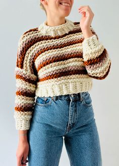 a woman is smiling and wearing a multicolored knit sweater with high rise jeans