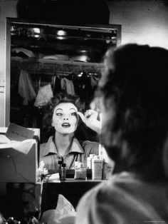 a black and white photo of a woman getting her hair done in front of a mirror