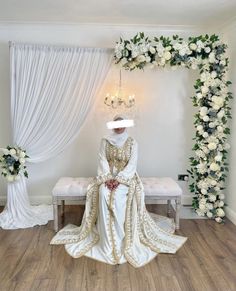 a white wedding dress sitting on top of a wooden floor next to a floral arch