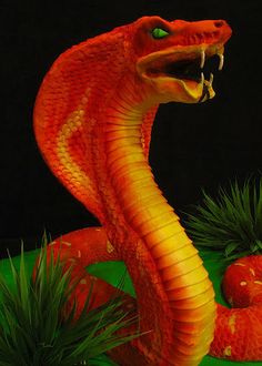 there is a fake snake on display in front of some plants and fruit, with its mouth open